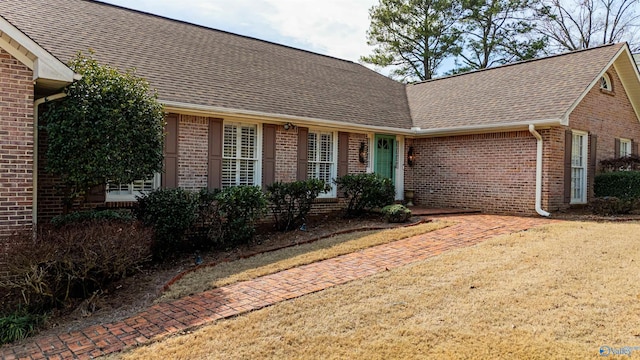 view of front facade featuring roof with shingles, a front yard, and brick siding