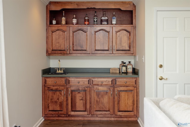 bar with a sink, indoor wet bar, dark wood finished floors, and baseboards