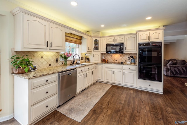 kitchen featuring dark wood-style floors, backsplash, a sink, light stone countertops, and black appliances