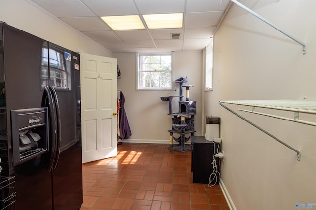 interior space with a paneled ceiling, brick floor, baseboards, and black fridge with ice dispenser