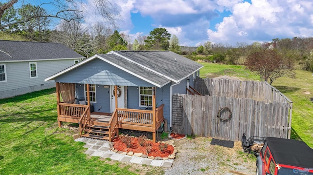 rear view of house with a shingled roof, covered porch, fence, and a yard