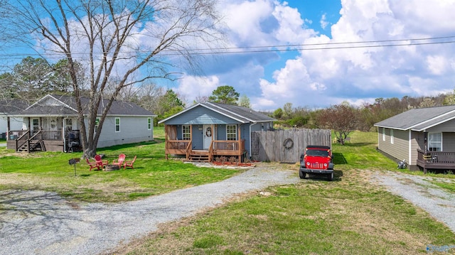 bungalow-style house featuring fence, gravel driveway, a deck, a front lawn, and a fire pit