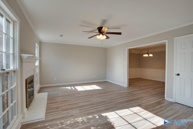 unfurnished living room featuring ceiling fan with notable chandelier, light hardwood / wood-style flooring, crown molding, and a fireplace