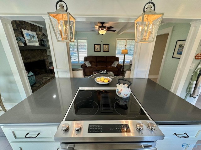 kitchen featuring stainless steel range, ceiling fan with notable chandelier, a stone fireplace, beam ceiling, and white cabinetry