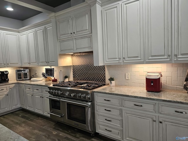 kitchen with tasteful backsplash, light stone countertops, white cabinets, and range with two ovens