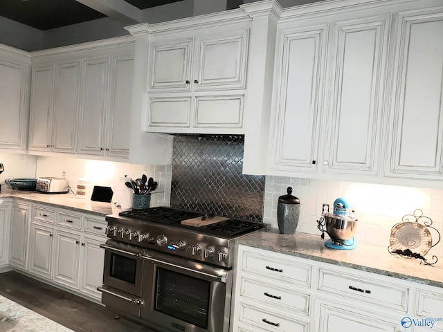 kitchen featuring tasteful backsplash, dark hardwood / wood-style flooring, light stone countertops, range with two ovens, and white cabinets