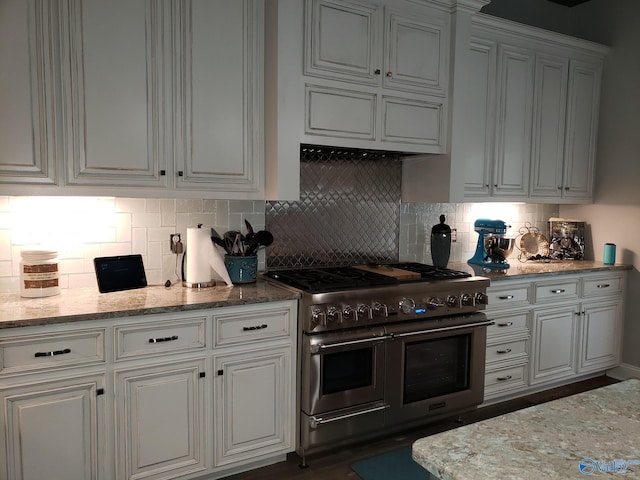 kitchen featuring white cabinetry, double oven range, light stone countertops, and decorative backsplash