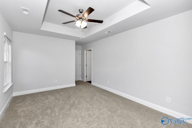 unfurnished room with a tray ceiling, light colored carpet, visible vents, and baseboards