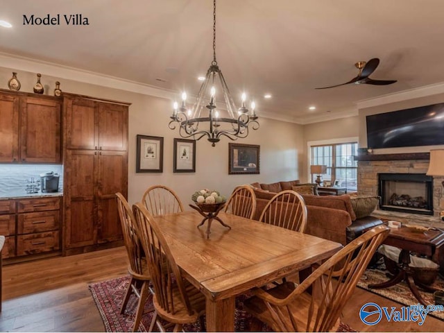 dining area with a fireplace, wood-type flooring, ceiling fan with notable chandelier, and ornamental molding