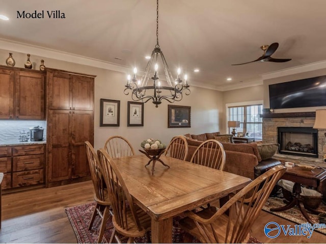 dining room featuring a stone fireplace, ornamental molding, a ceiling fan, and wood finished floors