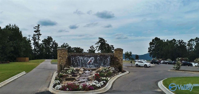 community sign featuring a lawn and uncovered parking