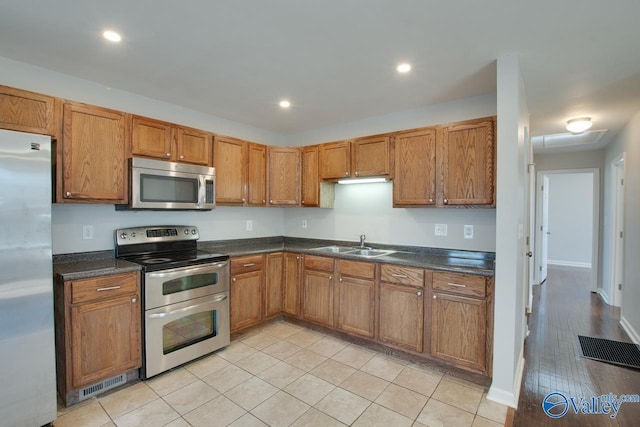 kitchen with recessed lighting, a sink, stainless steel appliances, dark countertops, and brown cabinets