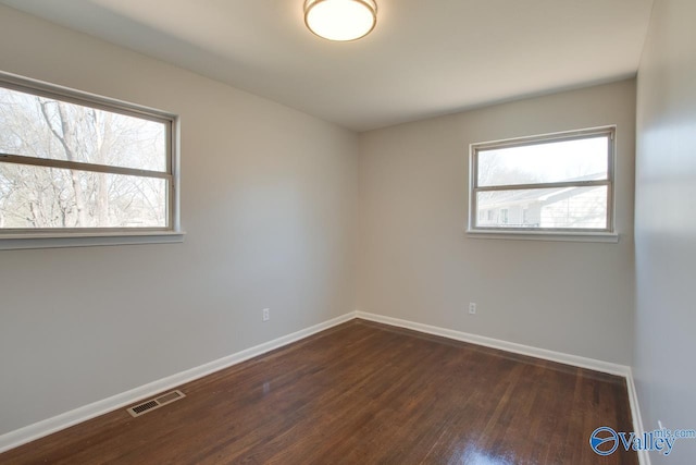 unfurnished room with visible vents, baseboards, and dark wood-style flooring