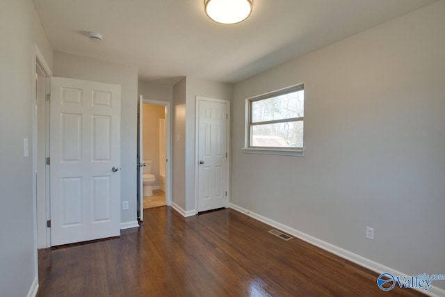 unfurnished bedroom with dark wood finished floors, visible vents, baseboards, and ensuite bathroom