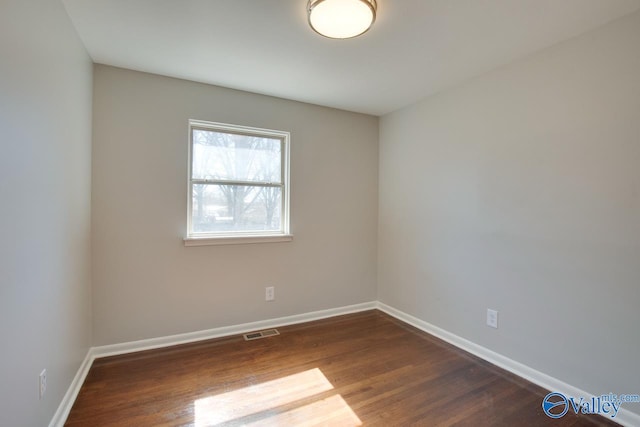 spare room with dark wood-style floors, visible vents, and baseboards