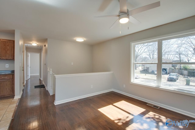 empty room featuring ceiling fan, visible vents, baseboards, and wood finished floors