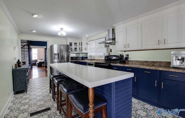 kitchen featuring white cabinetry, stainless steel refrigerator with ice dispenser, blue cabinetry, wall chimney range hood, and black / electric stove