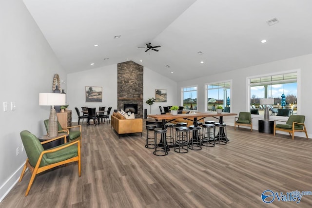 living area with wood finished floors, high vaulted ceiling, a stone fireplace, baseboards, and recessed lighting
