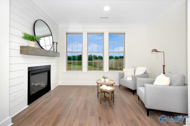 sitting room with a fireplace, wood finished floors, baseboards, and ornamental molding