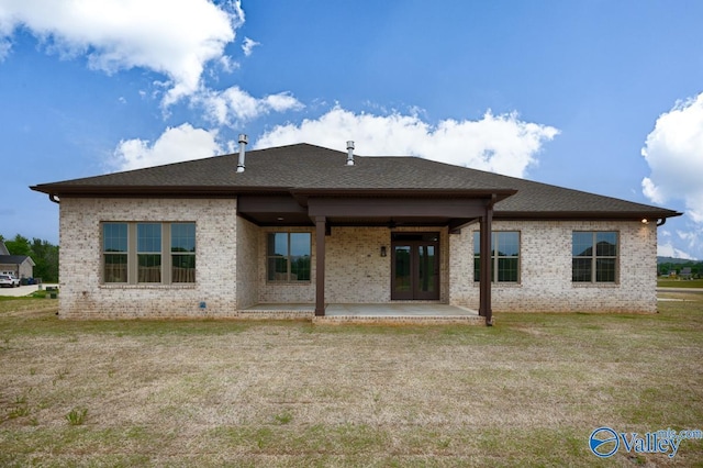 rear view of property with brick siding, a patio, a yard, and a shingled roof