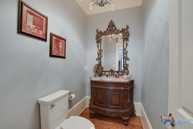 bathroom with an inviting chandelier, toilet, vanity, hardwood / wood-style flooring, and ornamental molding