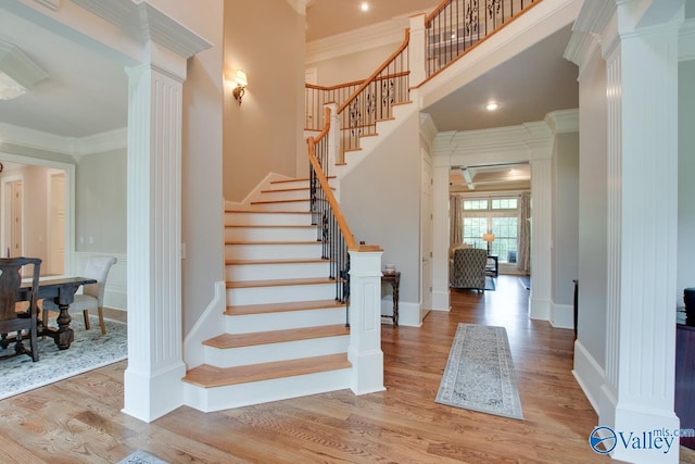 stairs featuring crown molding, wood-type flooring, decorative columns, and a high ceiling