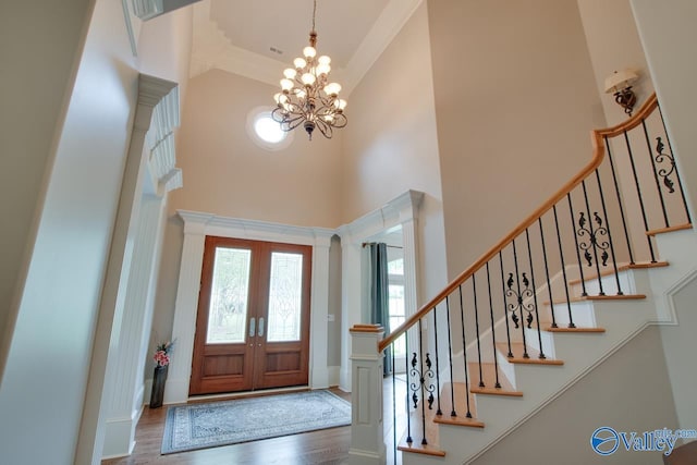 foyer with a towering ceiling, wood-type flooring, french doors, and a chandelier