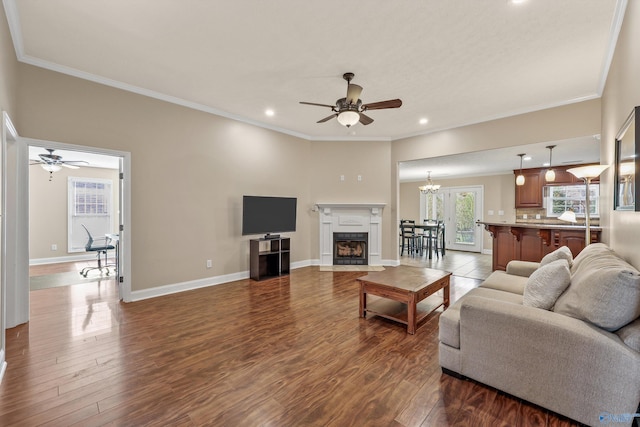 living room featuring ceiling fan with notable chandelier, wood-type flooring, and crown molding