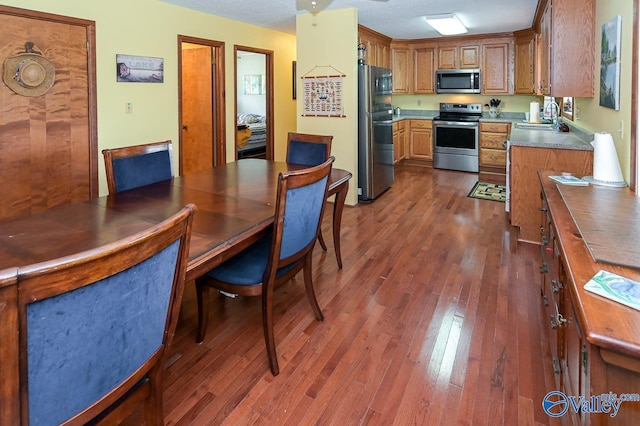 kitchen with brown cabinetry, dark wood-style floors, a sink, appliances with stainless steel finishes, and a textured ceiling
