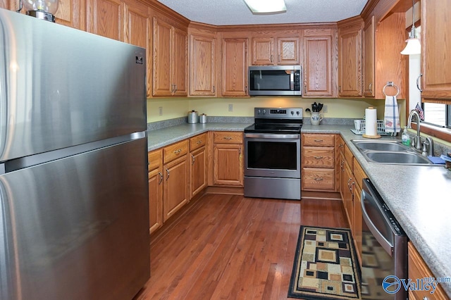 kitchen featuring sink, a textured ceiling, dark hardwood / wood-style flooring, hanging light fixtures, and stainless steel appliances