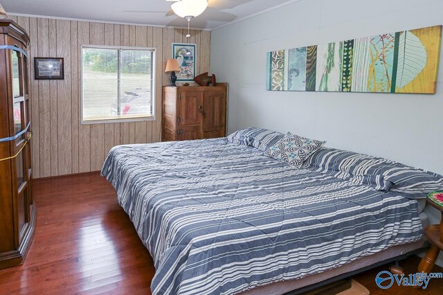 bedroom featuring crown molding, dark hardwood / wood-style floors, wooden walls, and ceiling fan