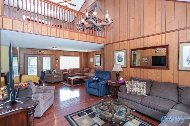 living room with high vaulted ceiling, wood-type flooring, wooden walls, and ceiling fan with notable chandelier