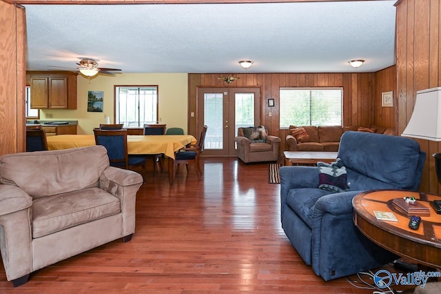 living room featuring wooden walls, wood finished floors, ceiling fan, french doors, and a textured ceiling