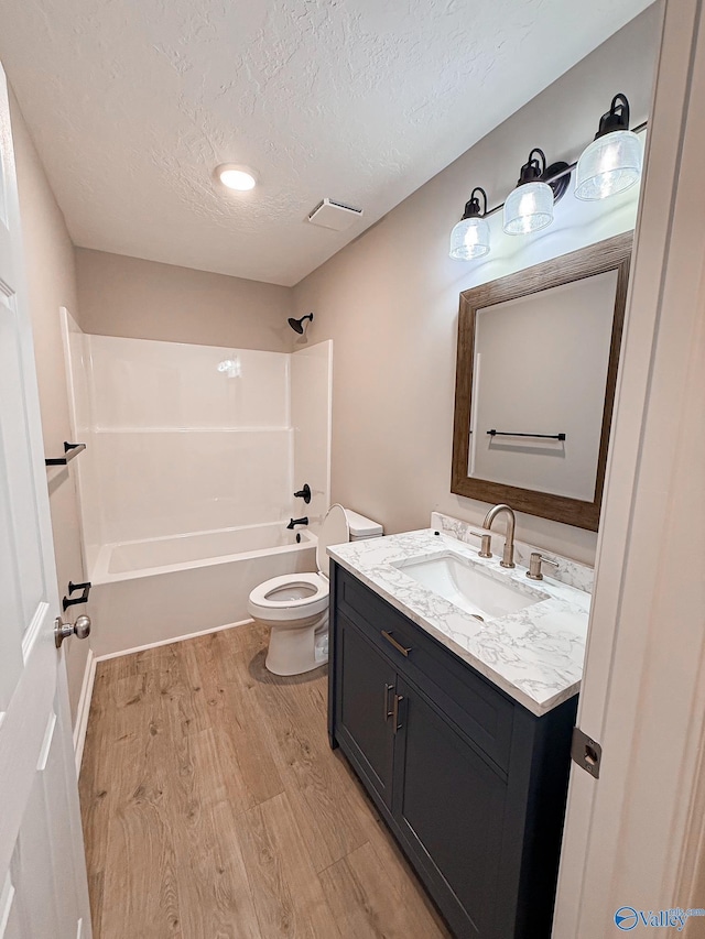 918 Wilson Ave, Gadsden, AL 35903 - bathroom featuring vanity, toilet, wood finished floors, a textured ceiling, and bathing tub / shower combination
