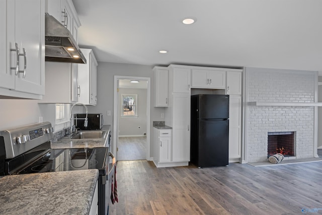 kitchen featuring black refrigerator, stainless steel range with electric stovetop, sink, and white cabinets