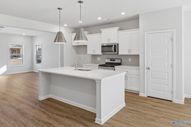 kitchen with a kitchen island with sink, a sink, light wood-style floors, appliances with stainless steel finishes, and white cabinets