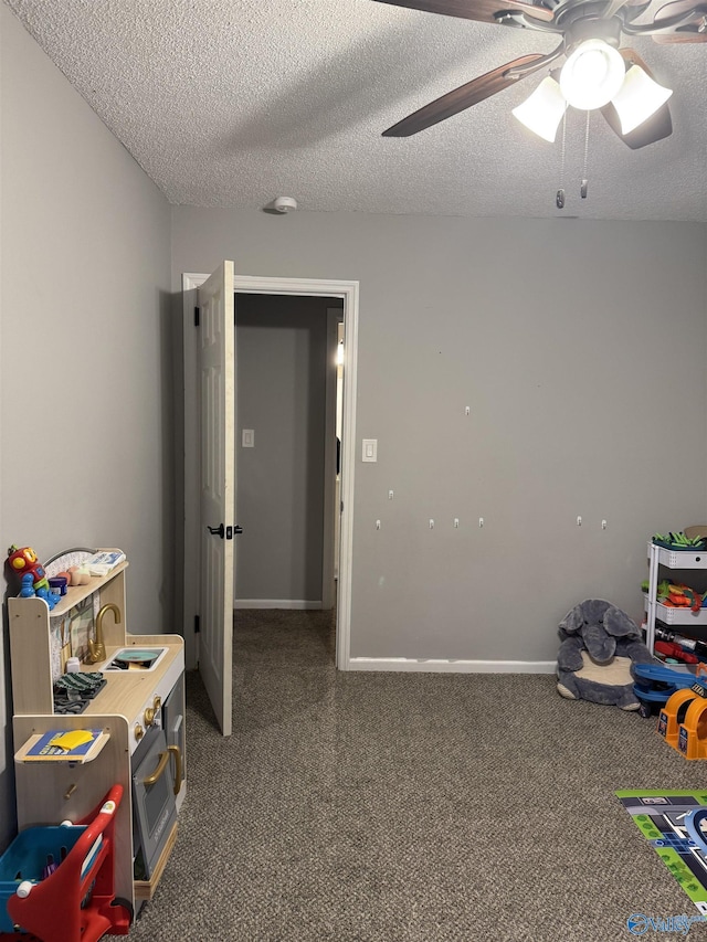 game room featuring dark colored carpet, ceiling fan, and a textured ceiling