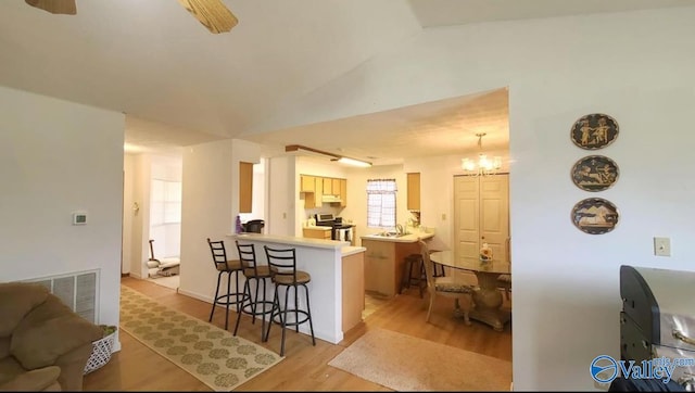 kitchen featuring kitchen peninsula, a kitchen breakfast bar, light hardwood / wood-style flooring, stainless steel electric range oven, and lofted ceiling