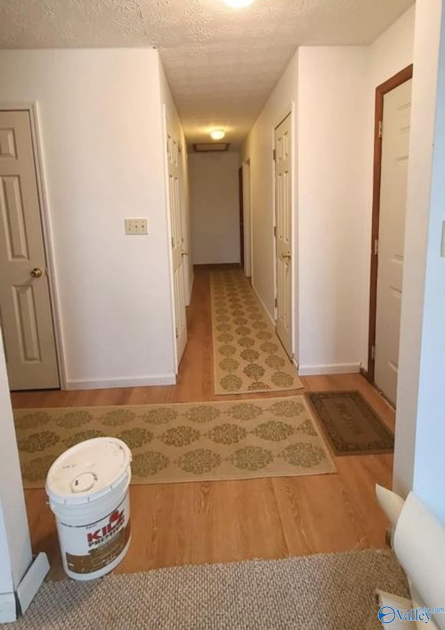 corridor with a textured ceiling and light hardwood / wood-style floors