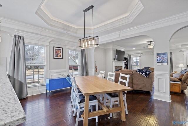 dining space featuring a tray ceiling, a stone fireplace, crown molding, and dark hardwood / wood-style floors