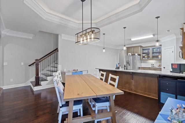 dining space with dark wood-type flooring, sink, crown molding, a tray ceiling, and a notable chandelier