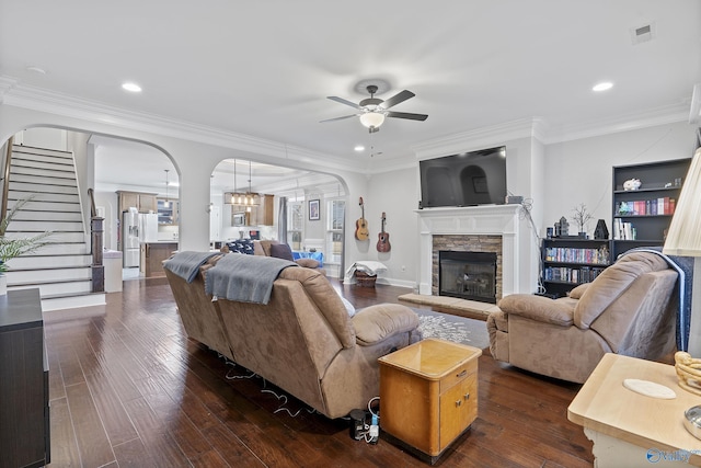 living room featuring a fireplace, ceiling fan with notable chandelier, dark wood-type flooring, and ornamental molding