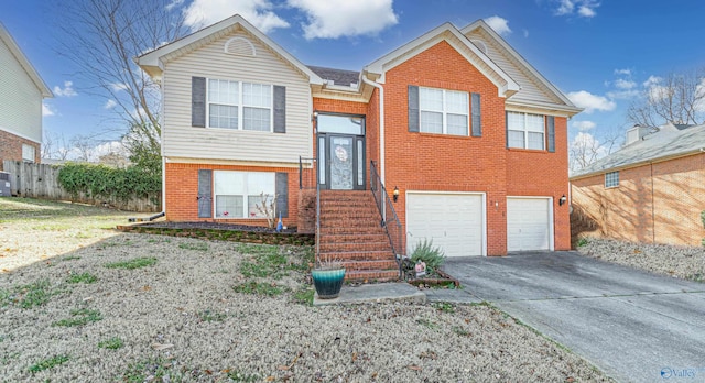 split foyer home with brick siding, concrete driveway, a garage, and fence