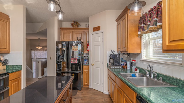 kitchen featuring dark wood finished floors, freestanding refrigerator, a sink, decorative backsplash, and dark countertops