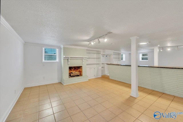 basement featuring a brick fireplace, crown molding, light tile patterned floors, rail lighting, and a textured ceiling