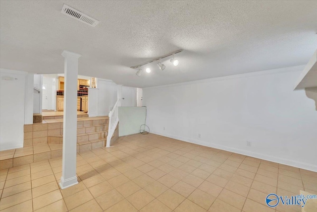 finished basement featuring visible vents, a textured ceiling, light tile patterned flooring, rail lighting, and baseboards