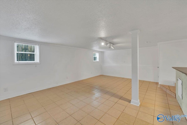 below grade area featuring track lighting, light tile patterned floors, baseboards, and a textured ceiling