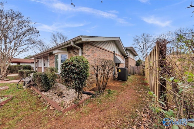 view of side of home featuring central AC unit, fence, and brick siding