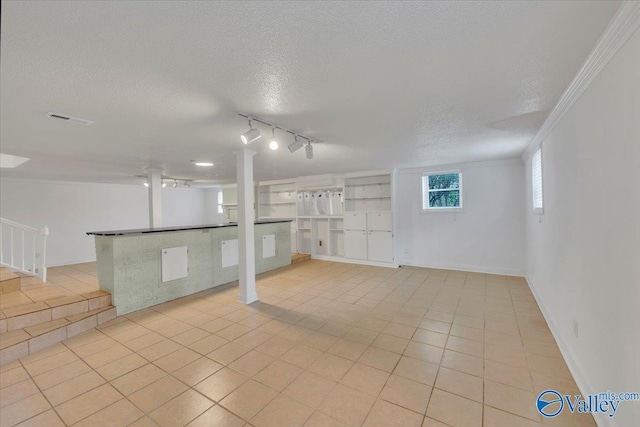 basement featuring visible vents, a textured ceiling, crown molding, light tile patterned floors, and baseboards