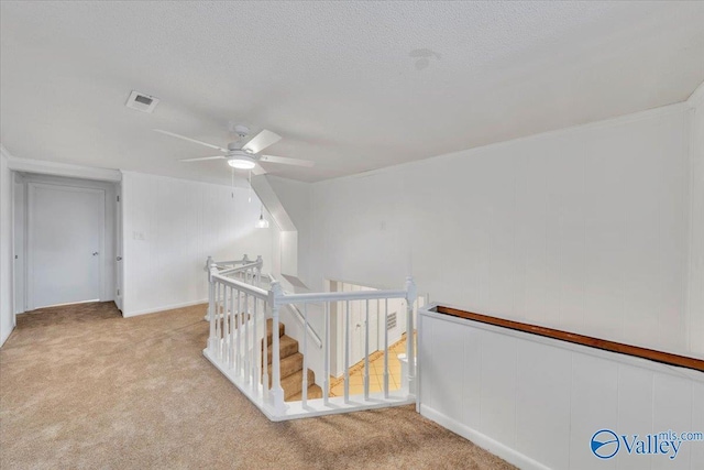 hallway featuring visible vents, an upstairs landing, a textured ceiling, and carpet flooring